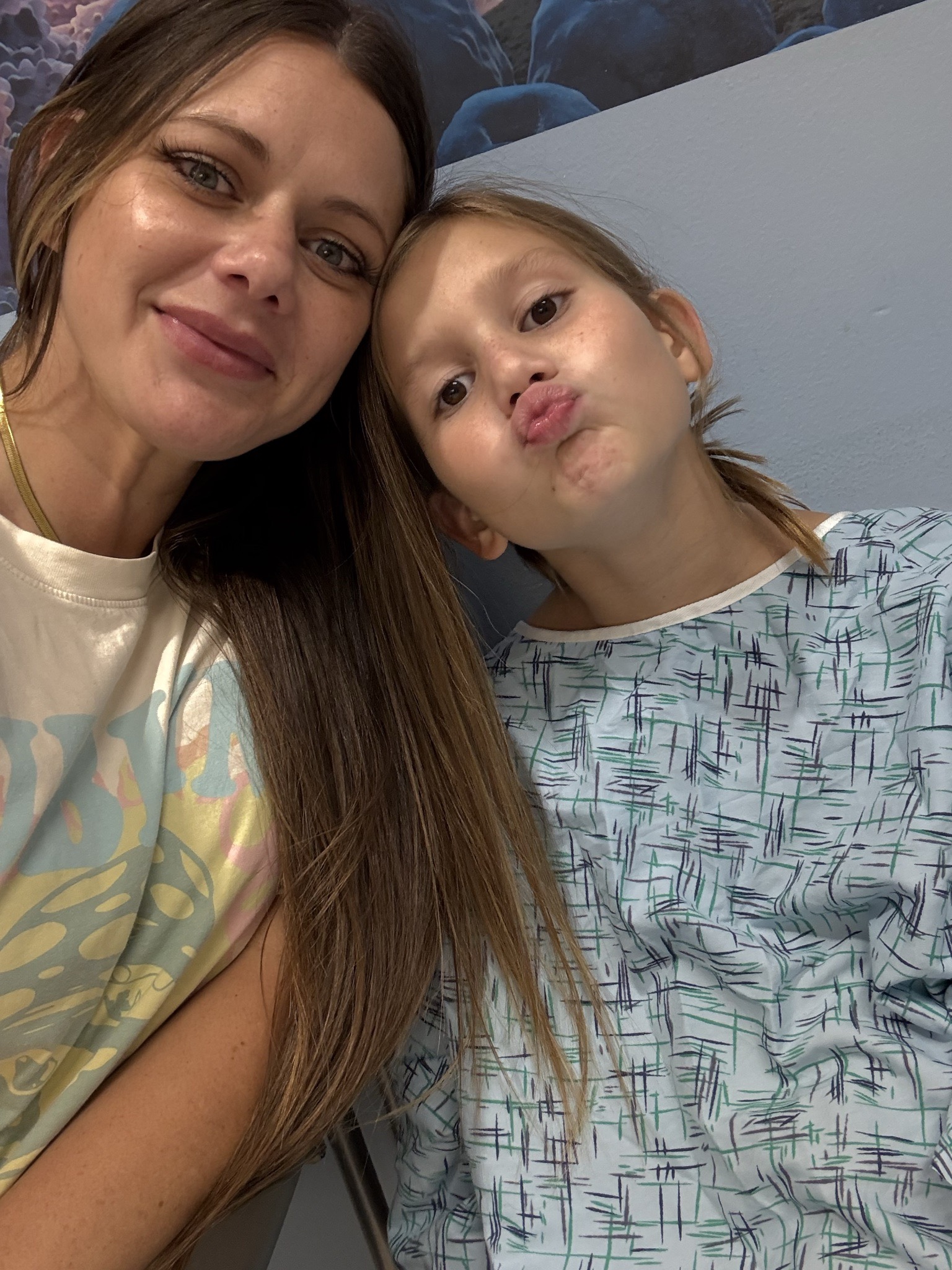 Audrey in a hospital gown playfully making a kiss face while taking a selfie alongside a family member.